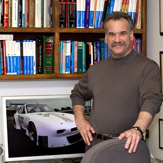 Professor Denmark standing in front of a bookshelf with an poster of a racecar